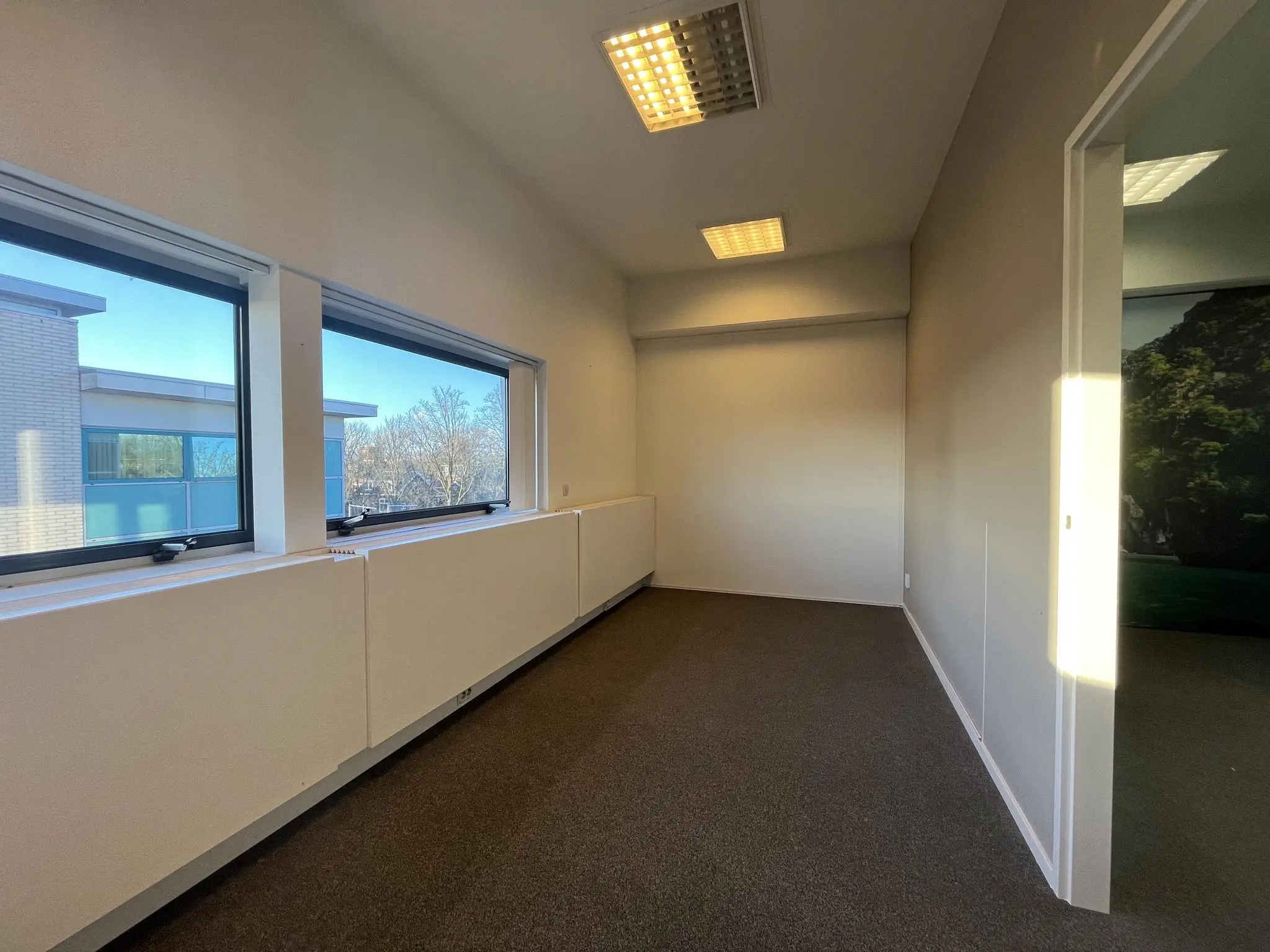 Licht en smal kantoorruimte in Leidse Rijn met twee ramen en uitzicht op naastgelegen gebouwen.